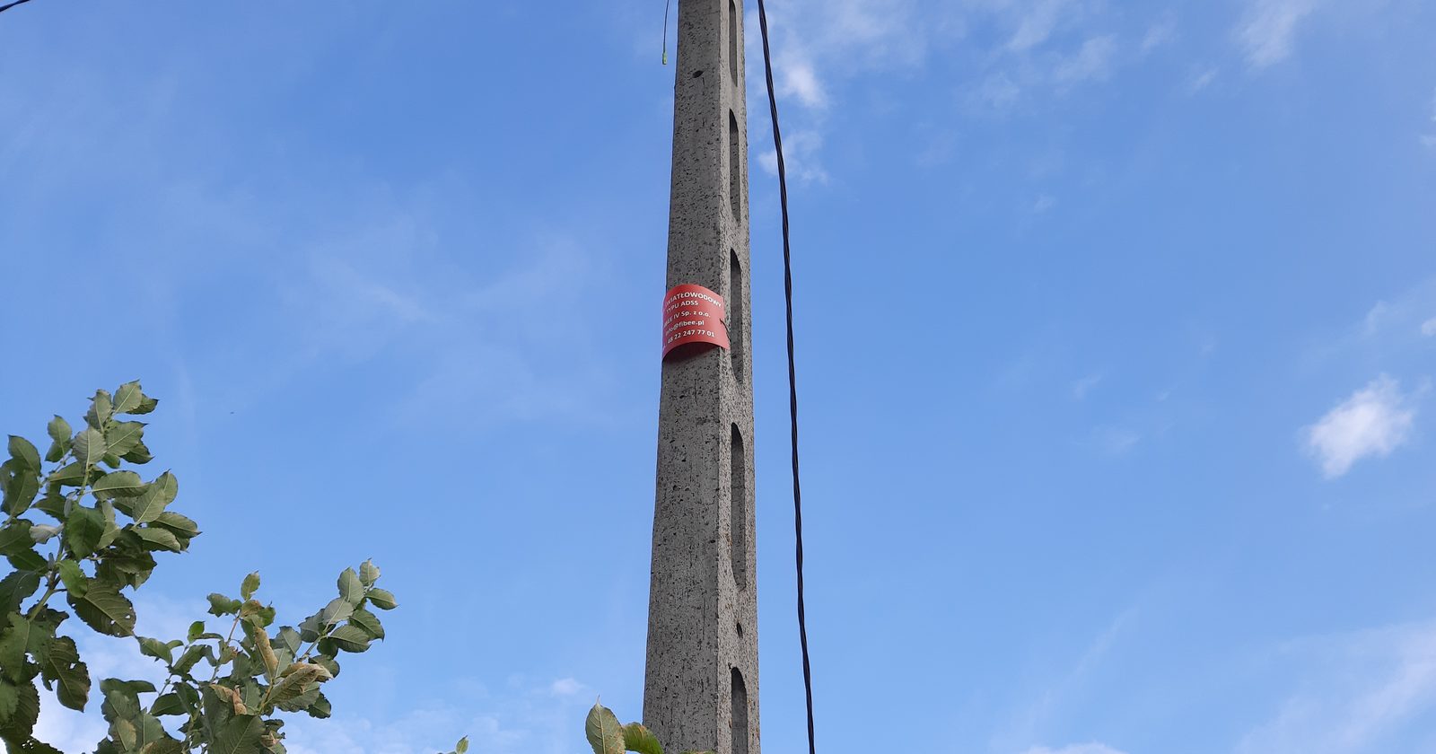 Napowietrzny światłowodowy kabel abonencki ze skrzynką przyłączeniową i zapasem kabla na słupie energetycznym na polskiej wsi.