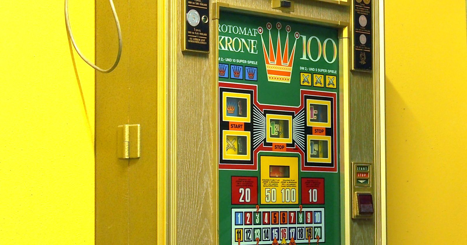 Zabytkowy automat do gier hazardowych Rotomat Krone 100 zawieszony na żółtej ścianie