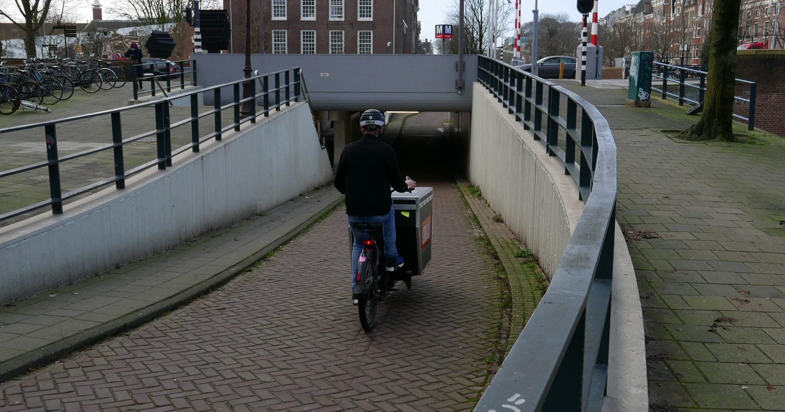 Kurier rowerowy z ładunkiem przejeżdżający przez tunel dla rowerzystów w Amsterdamie