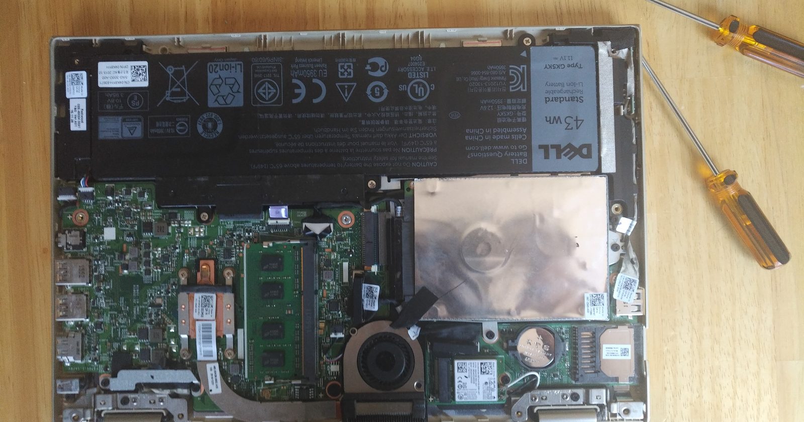 Laptop hybrydowy ze zdjętą tylną pokrywą, z widocznymi podzespołami i baterią podczas naprawy.